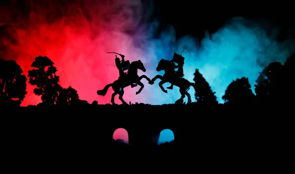 Medieval battle scene on bridge with cavalry and infantry. Silhouettes of figures as separate objects, fight between warriors on dark toned foggy background. Night scene. — Stock Photo, Image