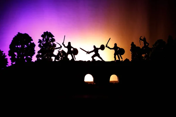 Cena de batalha medieval na ponte com cavalaria e infantaria. Silhuetas de figuras como objetos separados, luta entre guerreiros em fundo enevoado escuro. Cena noturna . — Fotografia de Stock