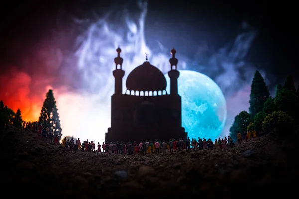 Silhouet van een grote menigte van mensen in bos bij nacht staande tegen een wazig moskee gebouw met getinte lichtstralen op mistige achtergrond. Ramadan Kareem achtergrond. — Stockfoto