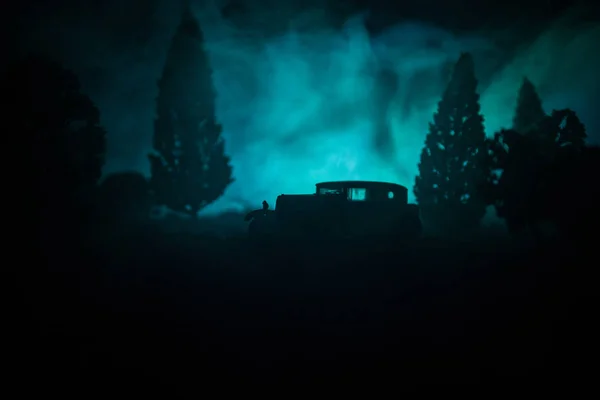 Silhouette eines alten Oldtimers im dunklen nebelfarbenen Hintergrund mit leuchtenden Lichtern bei wenig Licht oder Silhouette eines alten Autos im dunklen Wald. — Stockfoto