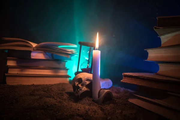 Secretária do Feiticeiro. Uma mesa iluminada pela luz da vela. Um crânio humano, livros antigos sobre a superfície da areia. Halloween fundo natureza-morta com um diferente elementos em fundo enevoado tonificado escuro . — Fotografia de Stock