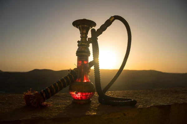 水烟, 传统阿拉伯语水管, 直接日落灯, 户外照片。日落背景下的水烟山背景或剪影。户外. — 图库照片