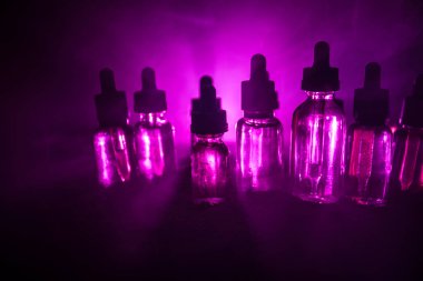 Vape kavramı. Duman bulutları ve vape sıvı şişe koyu arka plan üzerinde. Işık efektleri. Arka plan veya vape reklam veya vape arka plan olarak yararlı.