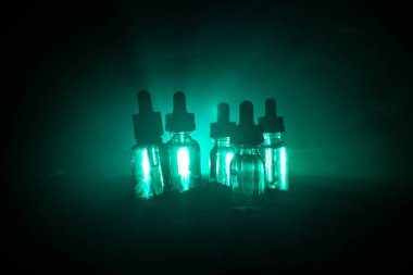 Vape kavramı. Duman bulutları ve vape sıvı şişe koyu arka plan üzerinde. Işık efektleri. Arka plan veya vape reklam veya vape arka plan olarak yararlı.