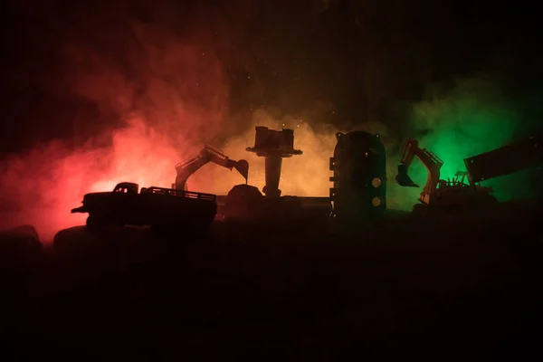 Sitio de construcción en una calle de la ciudad. Una excavadora amarilla estacionada durante la noche en un sitio de construcción. Decoración de mesa concepto industrial sobre fondo oscuro nebuloso tonificado — Foto de Stock