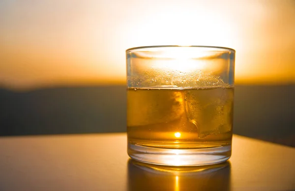 夕日を背景に山の風景を背景に劇的な夕焼けでウイスキーのショットの氷とウイスキーのガラス — ストック写真