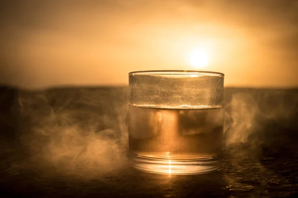 Ett glas whiskey med is på en solnedgång bakgrund eller skott av whisky på sunset dramatisk himmel på berg landskap bakgrund — Stockfoto