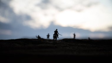 Dünya savaşı subayı (veya savaşçı) bir kılıç savaşmaya hazır ve karanlık sisli tonda arka plan üzerinde asker at üzerinde binici. Savaş alanı savaş alanı savaşan askerler.