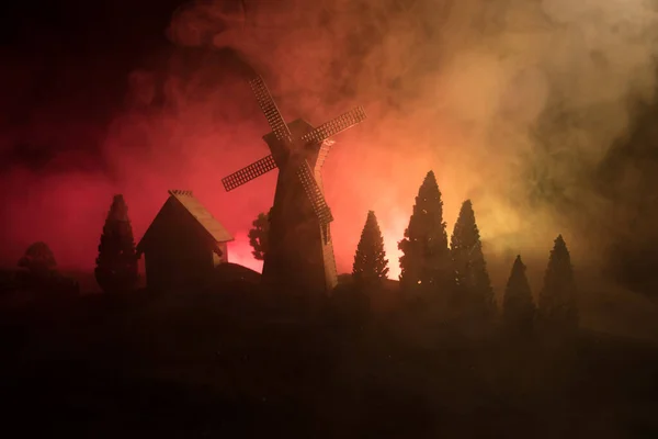 Windmühlensilhouette, die auf einem Hügel gegen den Nachthimmel steht. Nachtdekor mit alter Windmühle auf Hügel mit gruselig getöntem Nebelhintergrund mit Licht. — Stockfoto