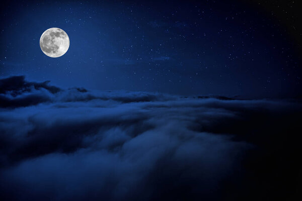 Full moon over clouds. Shone circle of the moon in darkness on a background of the star sky and clouds