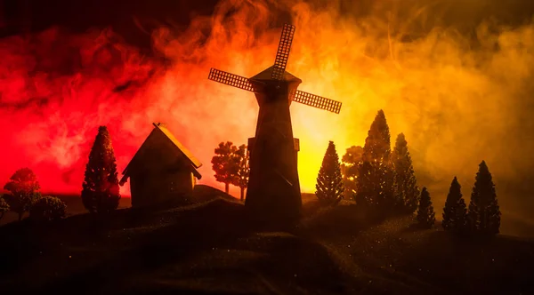 Väderkvarns siluett står på kullen mot natthimlen. Nattlig inredning med gammal väderkvarn på kulle med skräck tonad dimmig bakgrund med ljus. — Stockfoto