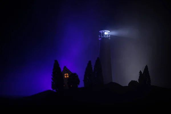 Lighthouse with light beam at night with fog. Old lighthouse standing on mountain. Table decoration. Toned background. Moonlighting.