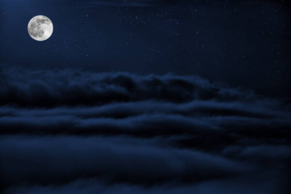Full moon over clouds. Shone circle of the moon in darkness on a background of the star sky and clouds
