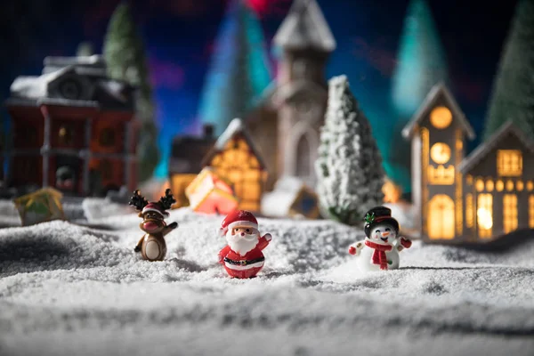 Conceito de Natal e feriados de Ano Novo. Pequenas casas pequenas decorativas bonitos na neve à noite no inverno, árvore de abeto em pé na neve com belas férias decoradas fundo — Fotografia de Stock