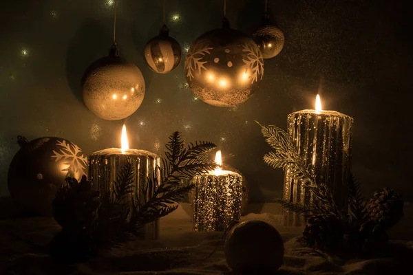 Decorazione artistica creativa. Decorazione natalizia con candele accese su sfondo scuro. Ornamenti natalizi su sfondo dorato scuro con luci . — Foto Stock