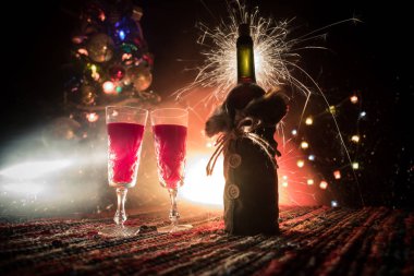 Kırmızı şarap kristal bardakta, renkli halıda şişe ve yaratıcı yeni yıl süslemeleri. Boşluğu kopyala