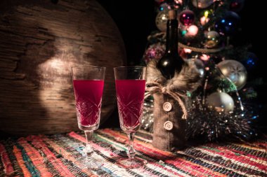 Kırmızı şarap kristal bardakta, renkli halıda şişe ve yaratıcı yeni yıl süslemeleri. Boşluğu kopyala