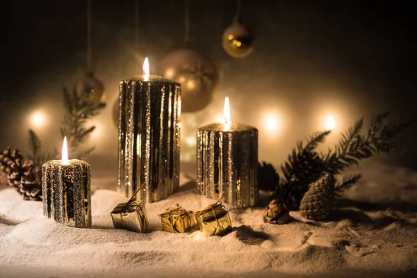 Decorazione artistica creativa. Decorazione natalizia con candele accese su sfondo scuro. Ornamenti natalizi su sfondo dorato scuro con luci . — Foto Stock