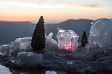Noel ve Yeni Yıl minyatürleri kar altında gün ışığında. Ağaçlı, karlı küçük bir oyuncak ev. Şenlik arka planı. Noel süslemeleri.