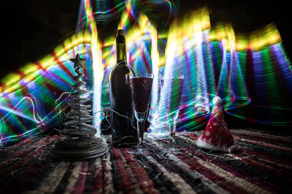 Kırmızı şarap kristal bardakta, renkli halıda şişe ve yaratıcı yeni yıl süslemeleri. Boşluğu kopyala — Stok fotoğraf