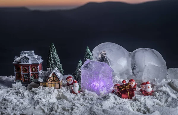 Χριστούγεννα και Πρωτοχρονιά μινιατούρα σπίτι στο χιόνι στο φως του ήλιου. Μικρό παιχνιδόσπιτο στο χιόνι με δέντρο. Εορταστικό φόντο. Χριστουγεννιάτικα στολίδια. — Φωτογραφία Αρχείου