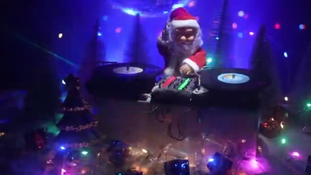 サンタクロース像とDjミキシングボードをカラフルなライトの下でクリスマスの組成物のクローズアップ映像 — ストック動画