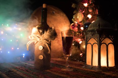 Kırmızı şarap kristal bardakta, renkli halıda şişe ve yaratıcı yeni yıl süslemeleri. Boşluğu kopyala