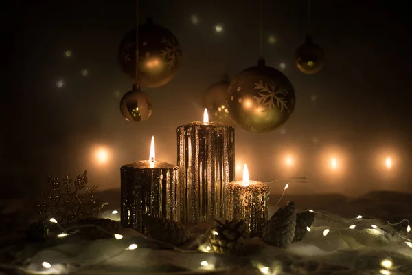 Decorazione artistica creativa. Decorazione natalizia con candele accese su sfondo scuro. Ornamenti natalizi su sfondo dorato scuro con luci . — Foto Stock