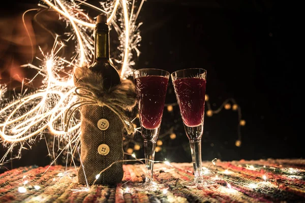 Czerwone wino w kryształowej szklance z butelką na kolorowym dywanie z twórczymi dekoracjami noworocznymi. Przestrzeń kopiowania — Zdjęcie stockowe