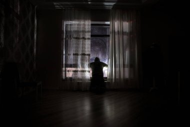 Odanın penceresinde duran bir adamın silüeti. Karanlık odanın penceresinde eski model bir fenerle çekilmiş fantezi bir resim..