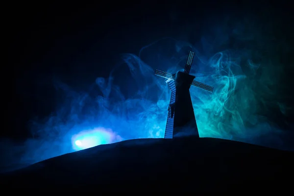 Windmolen silhouet staat op heuvel tegen de nachtelijke hemel. Nacht decor met oude windmolen op heuvel met horror toned mistige achtergrond met licht. — Stockfoto