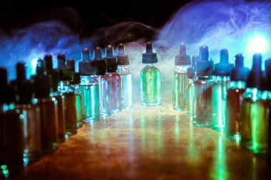Karanlık arka planda duman bulutları ve tüp sıvısı şişeleri. Işık efektleri. Arka plan, vape reklamı ya da vape arkaplan olarak kullanışlı. Seçici odak