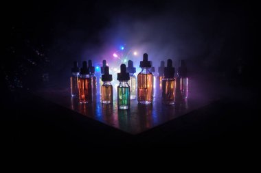 Karanlık arka planda duman bulutları ve tüp sıvısı şişeleri. Işık efektleri. Arka plan, vape reklamı ya da vape arkaplan olarak kullanışlı. Seçici odak