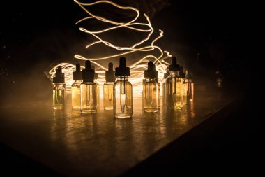 Karanlık arka planda duman bulutları ve tüp sıvısı şişeleri. Işık efektleri. Arka plan, vape reklamı ya da vape arkaplan olarak kullanışlı. Seçici odak