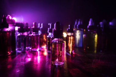 Karanlık arka planda duman bulutları ve tüp sıvısı şişeleri. Işık efektleri. Arka plan, vape reklamı ya da vape arkaplan olarak kullanışlı. Seçici odak