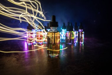 Karanlık arka planda duman bulutları ve tüp sıvısı şişeleri. Işık efektleri. Arka plan, vape reklamı ya da vape arkaplan olarak kullanışlı. Seçici odak