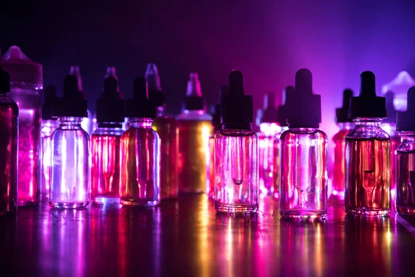 Smoke clouds and vape liquid bottles on dark background. Light effects. Useful as background or vape advertisement or vape background. Selective focus — 스톡 사진