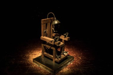 Death penalty electric chair miniature on dark. Creative artwork decoration. Image of an electric chair scale model on a dark backgorund clipart