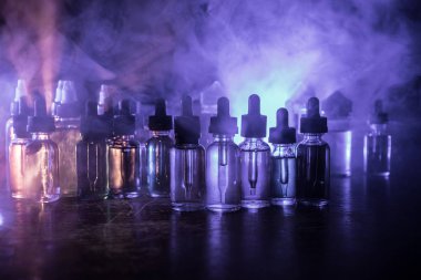 Vape konsepti. Karanlık arka planda duman bulutları ve tüp sıvısı şişeleri. Işık efektleri. Arka plan, vape reklamı ya da vape arkaplan olarak kullanışlı. Seçici odak