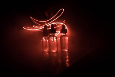 Vape konsepti. Karanlık arka planda duman bulutları ve tüp sıvısı şişeleri. Işık efektleri. Arka plan, vape reklamı ya da vape arkaplan olarak kullanışlı. Seçici odak