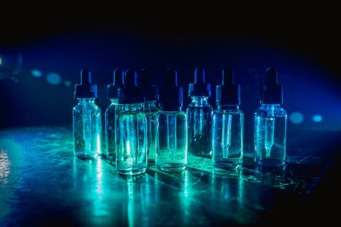 Vape konsepti. Karanlık arka planda duman bulutları ve tüp sıvısı şişeleri. Işık efektleri. Arka plan, vape reklamı ya da vape arkaplan olarak kullanışlı. Seçici odak