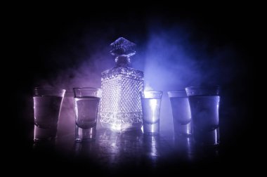 A beautiful carafe with vodka stands on a wooden table with glasses. Dramatic toned foggy background with light. Selective focus. Club drink concept.