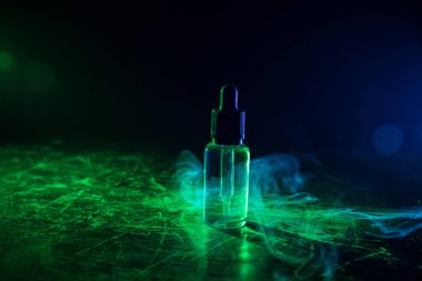 Vape konsepti. Karanlık arka planda duman bulutları ve tüp sıvısı şişeleri. Işık efektleri. Arka plan, vape reklamı ya da vape arkaplan olarak kullanışlı. Seçici odak
