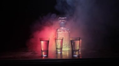 A beautiful carafe with vodka stands on a wooden table with glasses. Dramatic toned foggy background with light. Selective focus. Club drink concept.