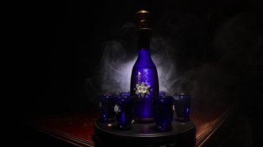 A beautiful blue carafe with vodka stands on a wooden table with glasses. Dramatic toned foggy background with light. Selective focus. Club drink concept.