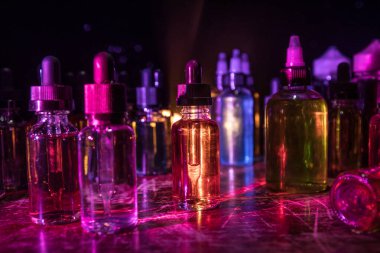 Vape konsepti. Karanlık arka planda duman bulutları ve tüp sıvısı şişeleri. Işık efektleri. Arka plan, vape reklamı ya da vape arkaplan olarak kullanışlı. Seçici odak
