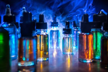 Vape konsepti. Karanlık arka planda duman bulutları ve tüp sıvısı şişeleri. Işık efektleri. Arka plan, vape reklamı ya da vape arkaplan olarak kullanışlı. Seçici odak