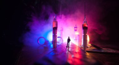 Narcotic drug problem concept. Silhouette of a man standing in the middle of the road on a misty night with giant Drug syringe and narcotic attributes. Creative artwork decoration