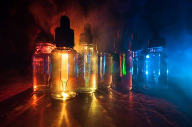 Vape konsepti. Karanlık arka planda duman bulutları ve tüp sıvısı şişeleri. Işık efektleri. Arka plan, vape reklamı ya da vape arkaplan olarak kullanışlı. Seçici odak