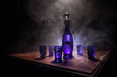 A beautiful blue carafe with vodka stands on a wooden table with glasses. Dramatic toned foggy background with light. Selective focus. Club drink concept.